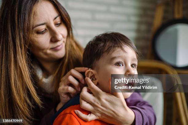 mother helping her son with his hearing aid - accessibility awareness stock pictures, royalty-free photos & images