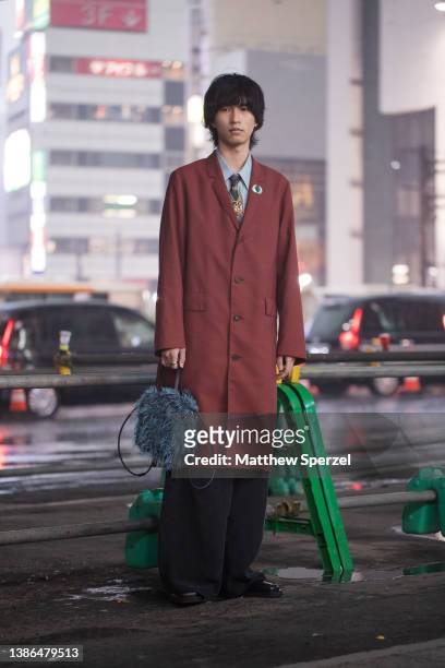 Guest is seen wearing maroon coat, collared shirt and tie, blue faux fur bag outside Shibuya Hikarie during Rakuten Fashion Week Tokyo 2022 A/W on...