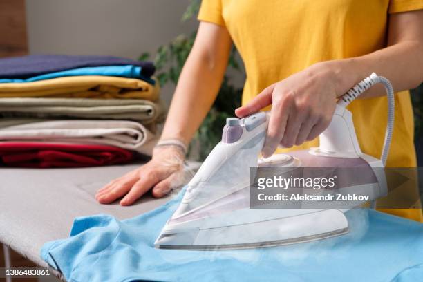 lots of bright, clean, multicolored pressed clothes stacked on the ironing board. a woman or a girl, a housewife, a cleaner or a housekeeper is ironing a t-shirt. the concept of homework, lack of time for household chores. women's duties, home life. - steam ironing bildbanksfoton och bilder