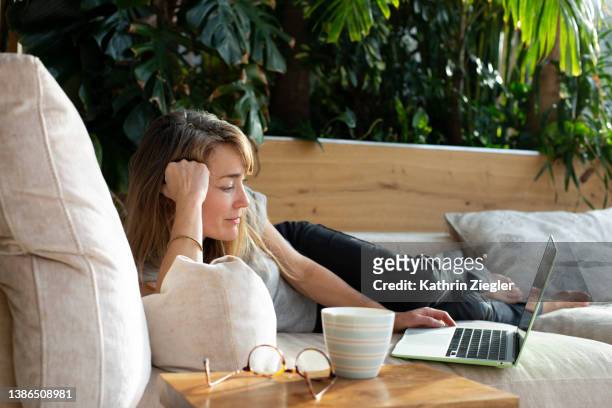 woman relaxing on sofa, watching a movie on laptop - donne bionde scalze foto e immagini stock