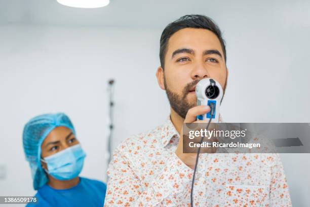 latin patient does respiratory tests by blowing into a medical device to measure the capacity of the lungs - menselijke rol stockfoto's en -beelden