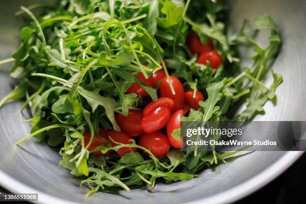 fresh green arugula leaves and halved red tomatoes in dish - rucola stock-fotos und bilder