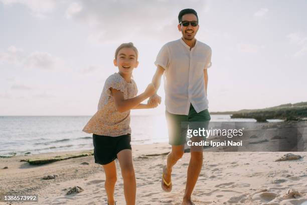 father and young daughter running on beach at sunset, japan - 家族　日本人　走る ストックフォトと画像