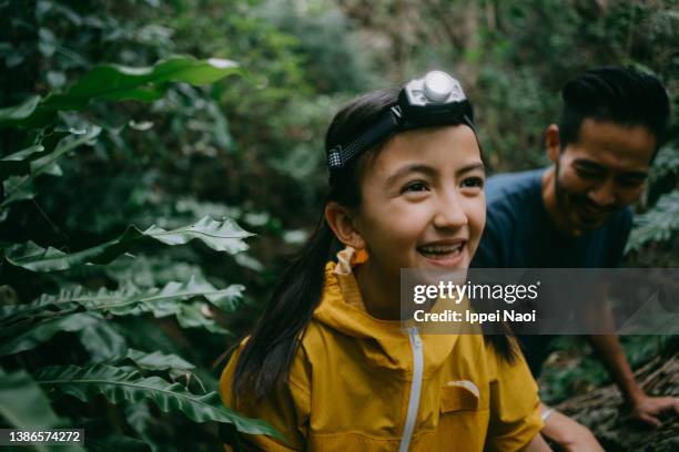 cheerful young girl with headlamp hiking through jungle cave - レインコート ストックフォトと画像
