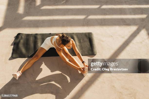 woman stretching on black yoga mat. warming up exercise, healthy lifestyle - sunny morning stock pictures, royalty-free photos & images