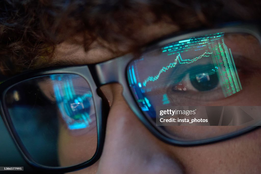 Young business man looking at trading charts reflecting in glasses, close up.