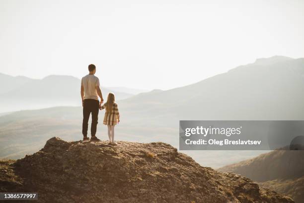 father and daughter together looking forward on beautiful mountain landscape. sustainable parenthood - family rear view stock pictures, royalty-free photos & images