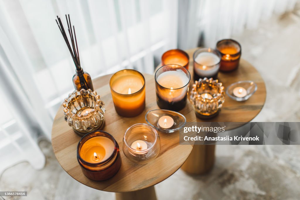 Scented candles in different candlelights on wooden table at home.