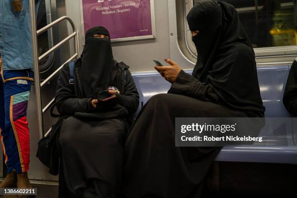 Two Muslim women wearing a full niqab veil read from their iPhones while riding in a subway car March 19, 2022 in New York City. Many daughters of...
