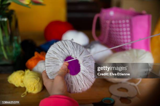 child threading wool around a cardboard circle to make pom-pom crafts at a table. - pom pom stock-fotos und bilder