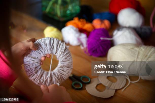 child threading wool around a cardboard circle to make pom-pom crafts at a table. - white pom pom stock pictures, royalty-free photos & images