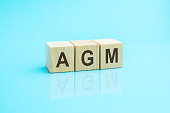 three wooden cubes with the letters AGM on the bright surface of a blue table