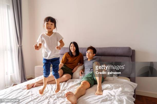 famiglia felice in camera da letto e bambina che salta sul letto. - materasso foto e immagini stock