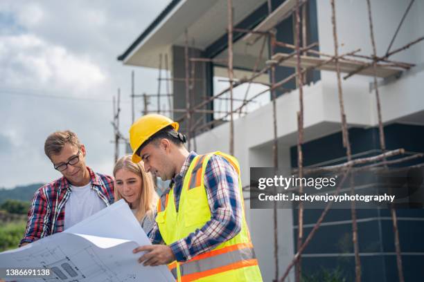 construction: young couple look at home plans with builder. - herbouwen stockfoto's en -beelden