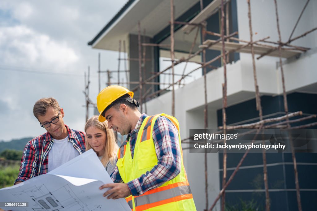 Construction: Young Couple Look At Home Plans with Builder.