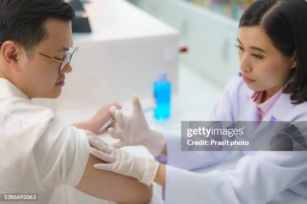 confident asian woman pharmacist prepares to give malaria, tetanus, typhoid, hepatitis vaccine young to man. - hepatitis a photos et images de collection
