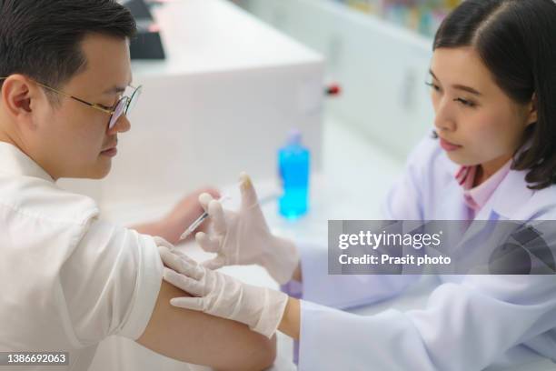 confident asian woman pharmacist prepares to give malaria, tetanus, typhoid, hepatitis vaccine young to man. - hepatitis stock pictures, royalty-free photos & images