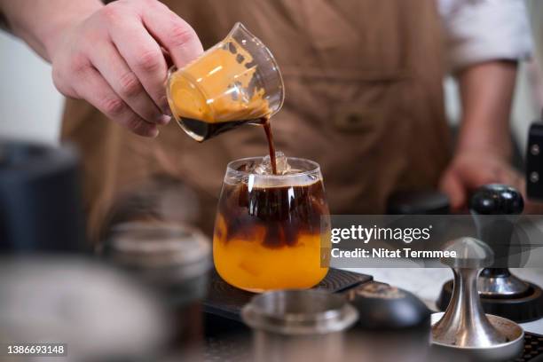 iced americano orange juice. close-up shot of a male barista pouring americano coffee mixed with orange juice into a glass. - orangensaft stock-fotos und bilder