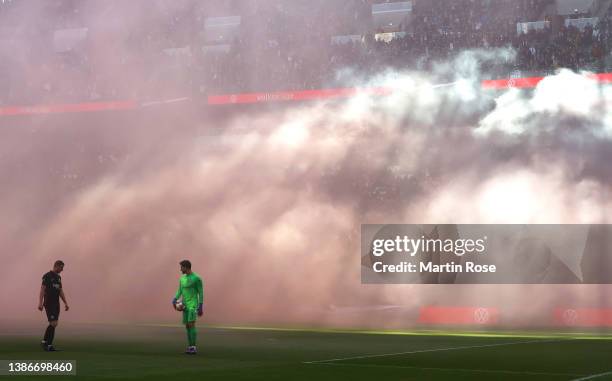 Smoke from flares spreads across the stadium as Kevin Trapp of Eintracht Frankfurt waits to restart play during the Bundesliga match between RB...