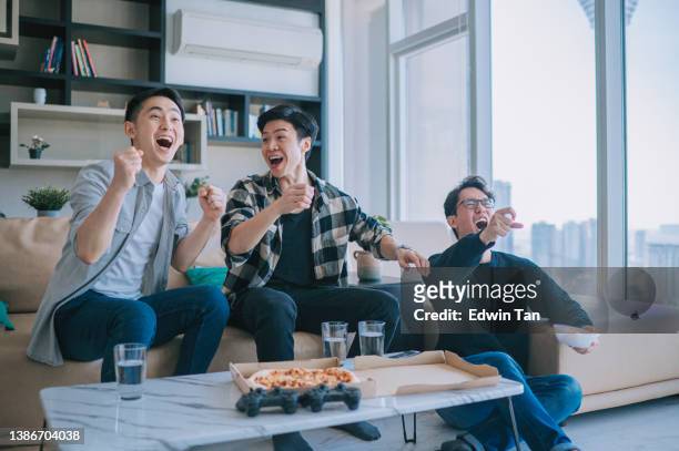 asian chinese young man shouting and cheering for his team support while watching sports on tv from home with his friends. celebrate victory when sports team wins championship. friends cheer, shout - watching stock pictures, royalty-free photos & images