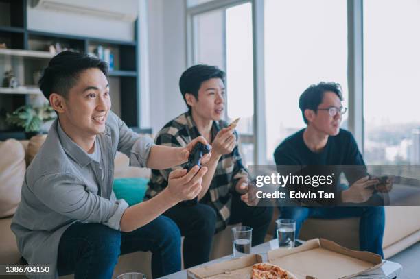 asian chinese young man enjoy playing video games with his friend in living room during weekend - adrenaline junkie stock pictures, royalty-free photos & images