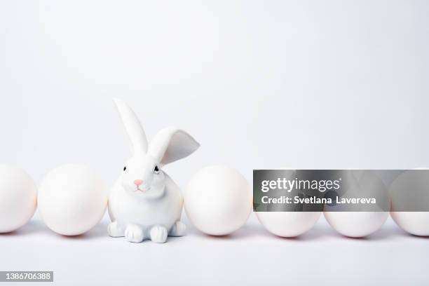 a row of many white eggs and one toy rabbit on white background. easter holiday concept. monochrome background. - paasontbijt stockfoto's en -beelden