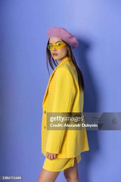 stylish fashion model woman in yellow jacket and skirt on purple background looking at camera. lady in the studio in a new collection of summer trendy clothes. - skirt suit stock-fotos und bilder