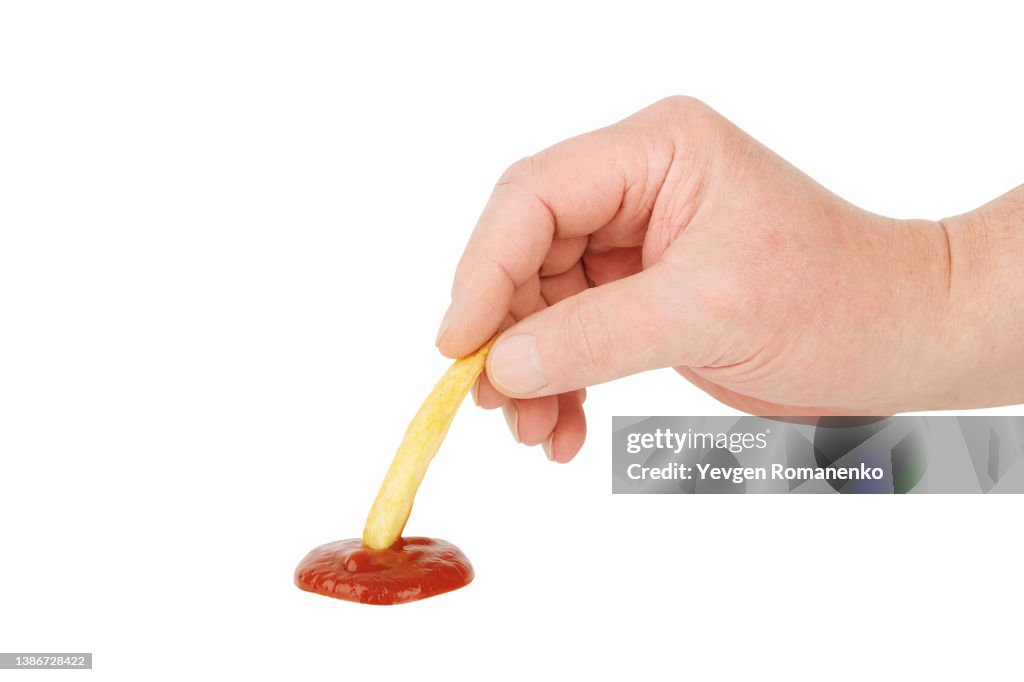 Closeup of mans hand dipping French fry in ketchup