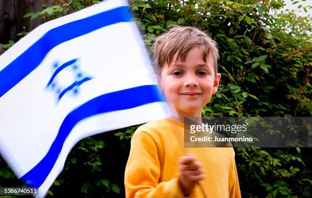 lächelnder kaukasischer junge, der eine israelische flagge schwenkt und in die kamera schaut - judentum stock-fotos und bilder