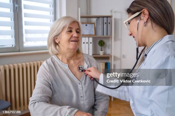 beautiful doctor examines senior woman heartbeat at the doctor's office - lung doctor patient stockfoto's en -beelden