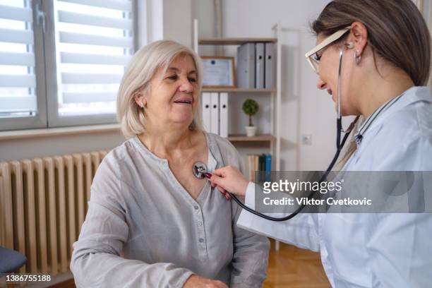 beautiful doctor examines senior woman heartbeat at the doctor's office - listening to heartbeat 個照片及圖片檔