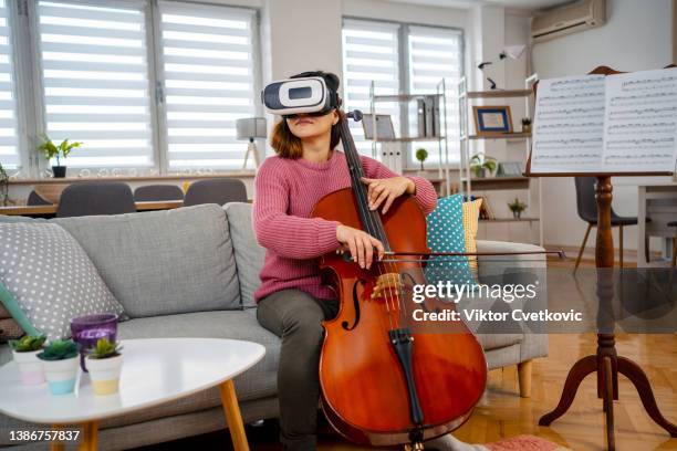 young woman experiencing virtual reality of a sold out concert while playing violoncello at home - virtual concert stock pictures, royalty-free photos & images