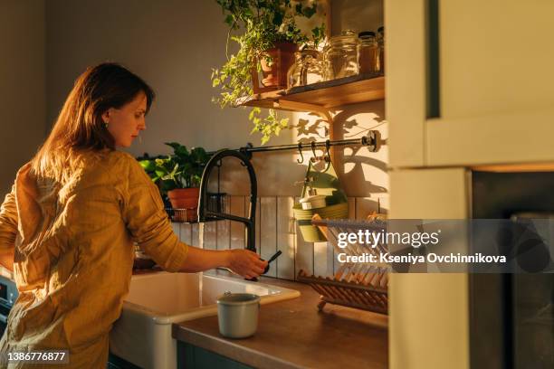 close up shot of a woman washing a frying pan with a cleaning liquid under tap water. using dishwasher in a modern kitchen. natural clean diet and healthy way of life concept. - sunny kitchen stock pictures, royalty-free photos & images