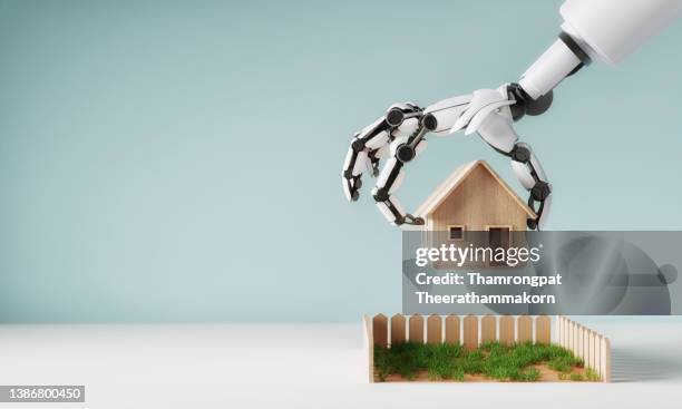 robotic arm is moving the model home onto the lawn ground surrounding house. business investment and house mortgage concept. innovative technology of artificial intelligence theme. - new testament stockfoto's en -beelden