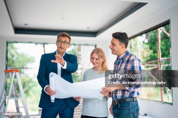 happy couple talking while having a meeting with their architect at construction site. - mid adult stock pictures, royalty-free photos & images