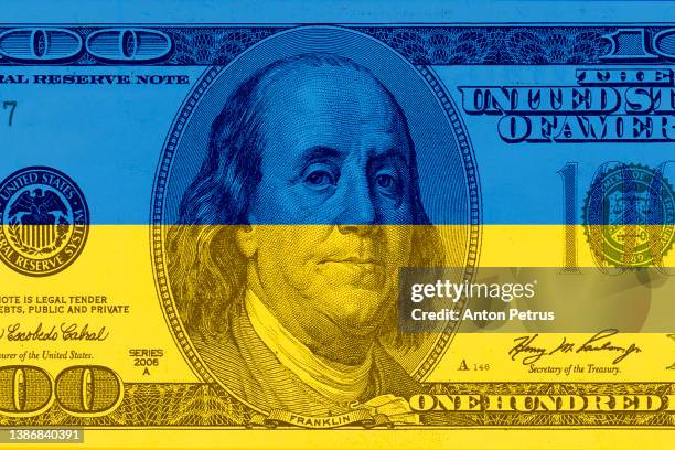 one hundred dollar bill on the background of the ukrainian flag - unidade monetária dos estados unidos imagens e fotografias de stock