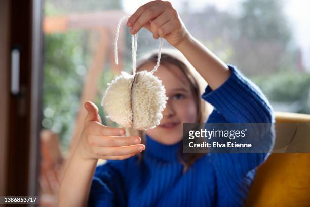 girl (8-9) holding up an incomplete homemade pom-pom ball made from cream coloured wool. - wool ball stock-fotos und bilder