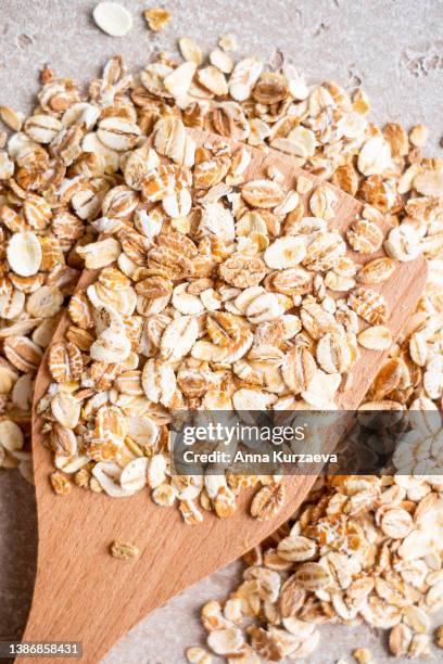 close-up of raw oat flakes in a wooden spoon and on a table, top view. healthy grains. - floco de aveia imagens e fotografias de stock