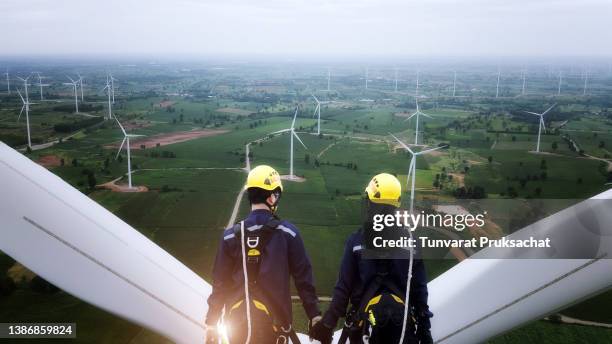 two electric engineer wearing personal protective equipment working on top of wind turbine farm. - wind power stock-fotos und bilder