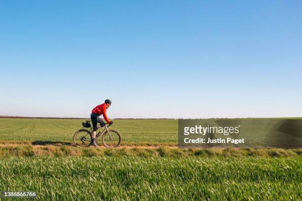 cyclist on gravel track through agricultural fields - groen jak stockfoto's en -beelden