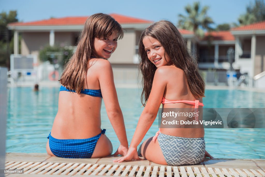Cheerful Young Girls Sitting On The Edge Of A Swimming Pool High
