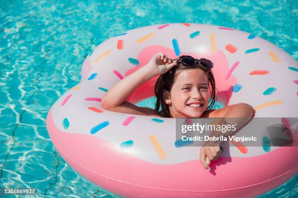 fille flottant dans un anneau gonflable à la piscine et enlevant des lunettes de soleil - ado en maillot de bain photos et images de collection