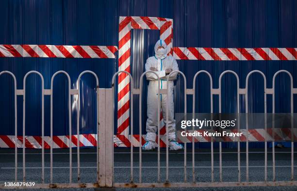 Guard wears a protective suit as he watches over a barricaded community that was locked down for health monitoring after recent cases of COVID-19...