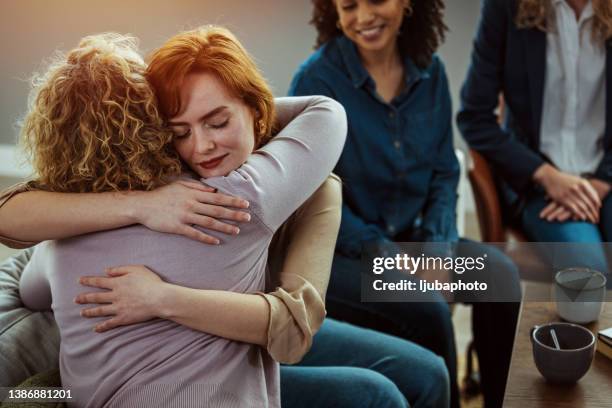a young woman receives a hug from the woman sitting next to her during group therapy. - repentant stock pictures, royalty-free photos & images