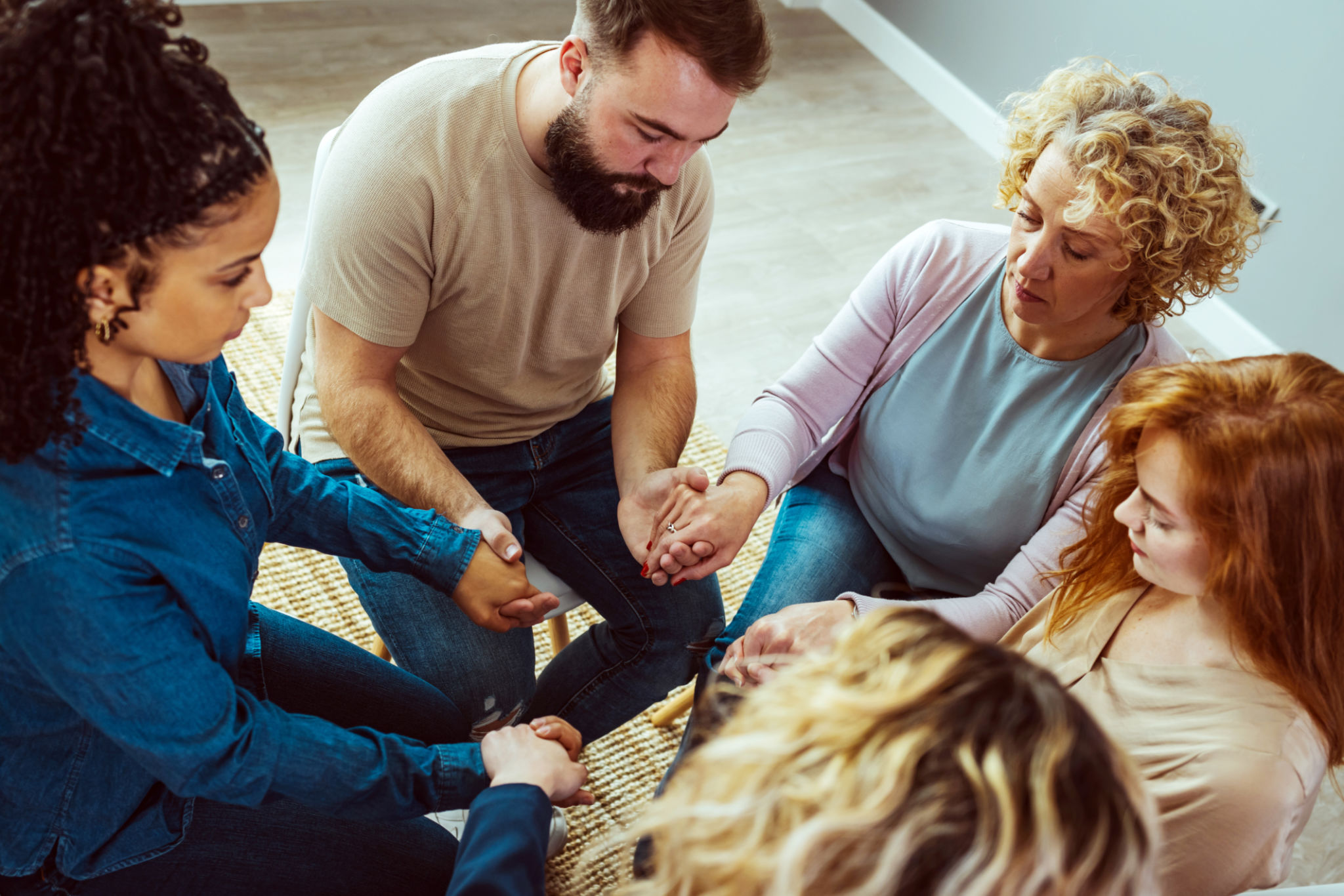 Close-up of a group of diverse people sitting in a circle and holding hands together during a support group meeting Close-up of a group of diverse people sitting in a circle and holding hands together during a support group meeting