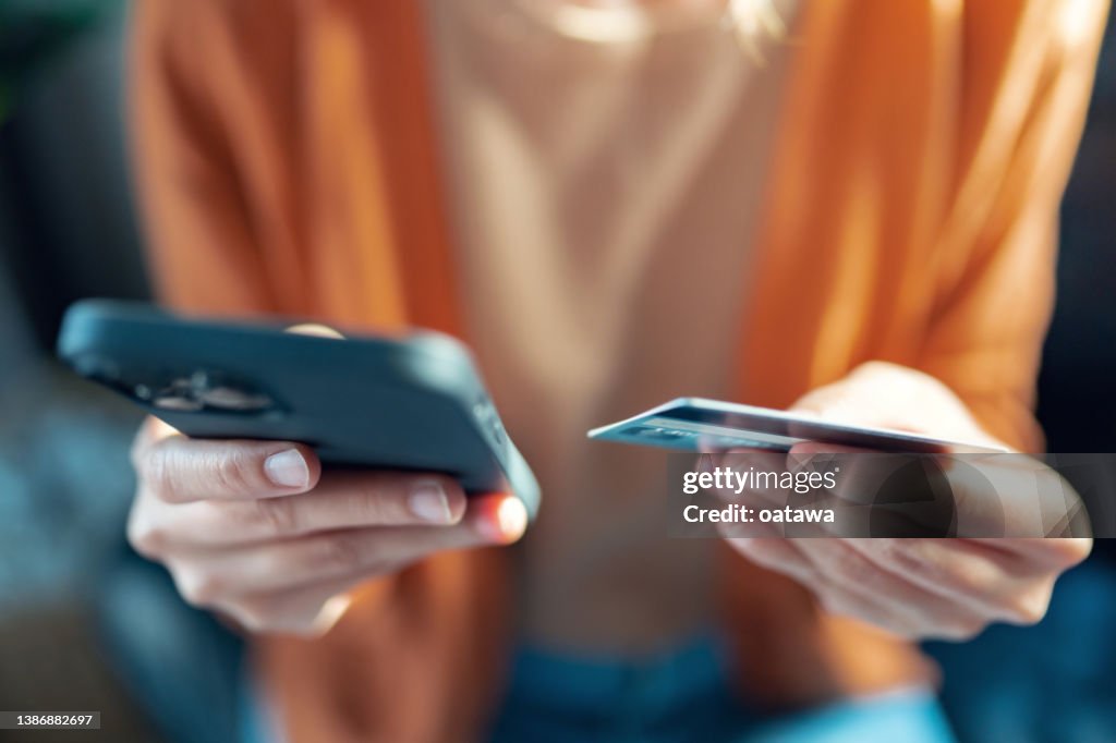 Mains d’une femme tenant une carte de crédit et utilisant un téléphone intelligent pour les achats en ligne