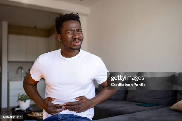 junger afroamerikaner, der sich zu hause krank fühlt - men stomach pain stock-fotos und bilder