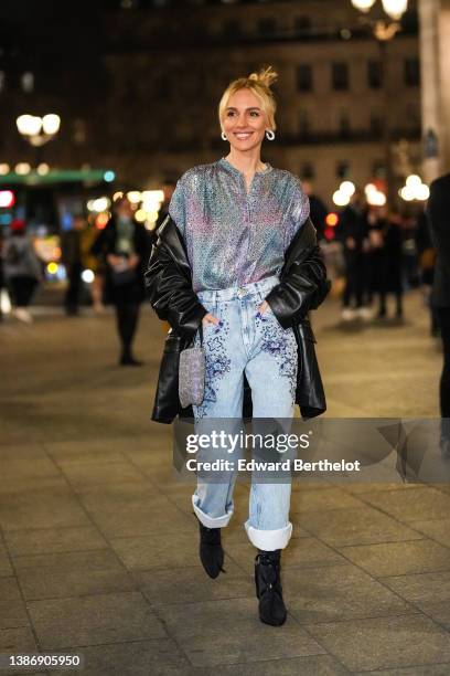 Viktoria Rader wears silver and diamonds earrings, a silver with blue and purple shiny reflect / embossed pattern shirt, a black shiny leather coat,...