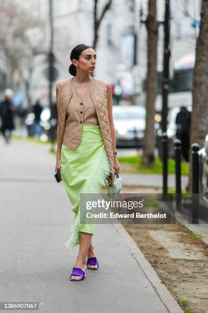 Gabriella Berdugo wears gold earrings, a silver chain pendant necklace, a beige brown with small pink and green flower print pattern buttoned /...