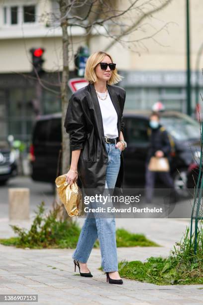 Lisa Aiken wears black sunglasses, a gold large chain necklace, a white t-shirt, a black shiny leather jacket, a silver watch, a gold large chain...